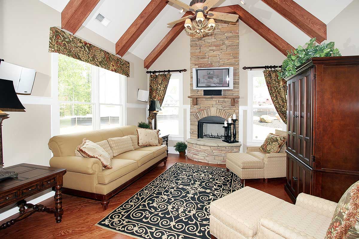 Living room with vaulted ceiling, exposed beams, stone fireplace with TV, and large windows.
