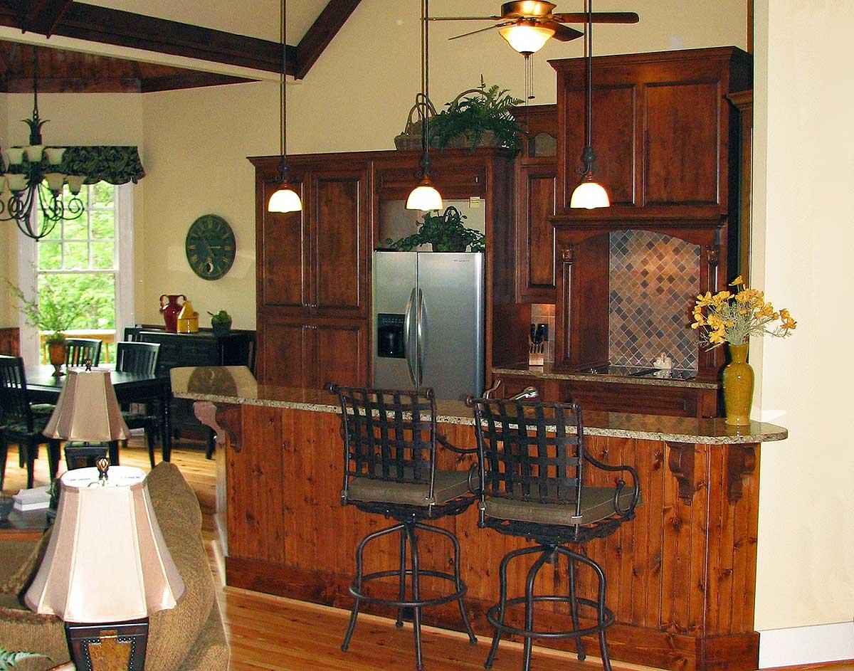 Kitchen with dark wood cabinets, granite countertop island, stainless steel refrigerator, and vaulted ceiling with exposed beams.