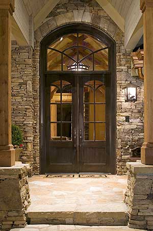 Exterior: double arched doors with transom window, stone facade, and covered entryway with wooden columns.