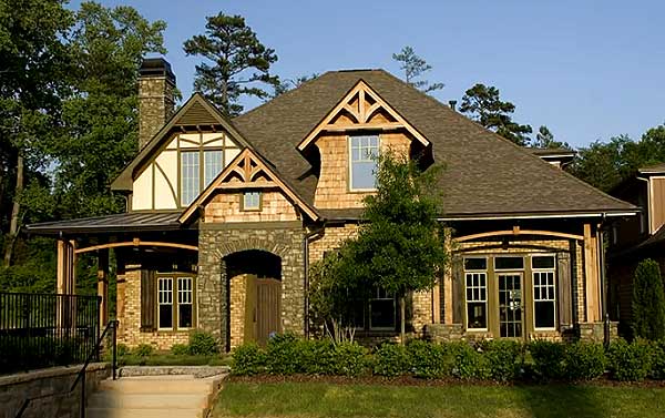 House plan exterior featuring Tudor-inspired gables, stone archway entrance, stone chimney, and covered porch.