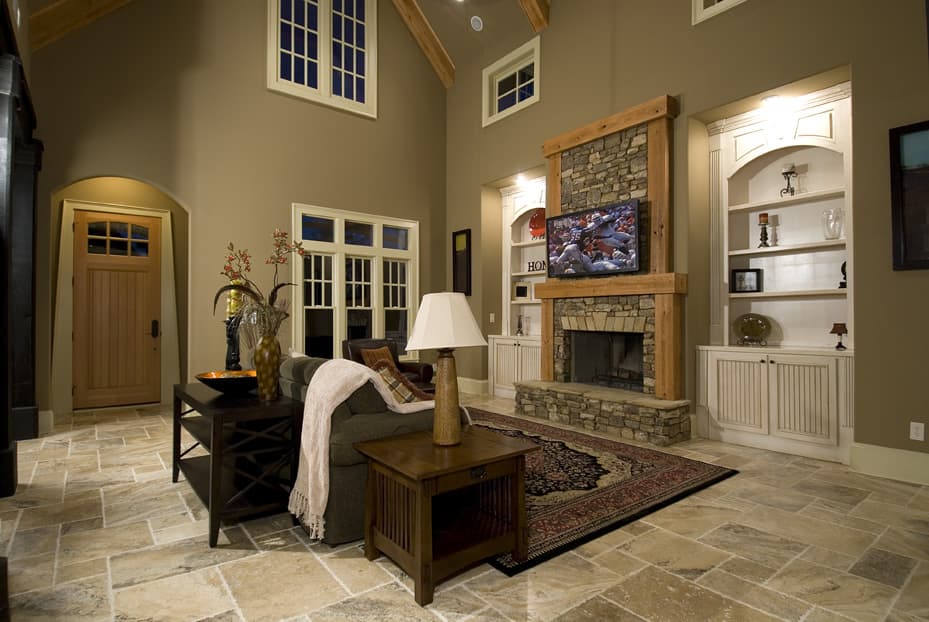 Great room with vaulted ceiling, stone fireplace with timber surround, built-in shelving, and wood door.
