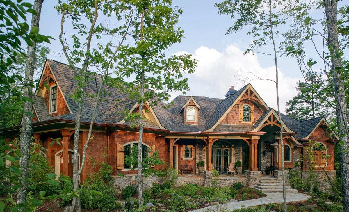 House plan exterior: Wood shingle siding, stone foundation, multiple gables, covered front porch with timber framing.