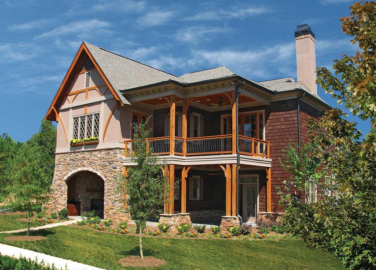 House plan exterior with stone arched entrance, second-story deck with wooden posts and railings, and shingle siding.