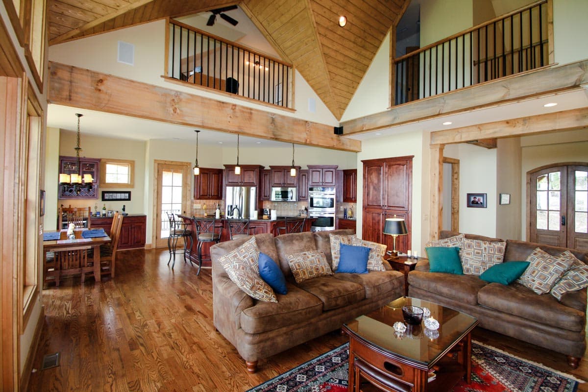 Great room with vaulted wood-paneled ceiling, exposed beams, fireplace, kitchen island, and loft overlooking the space.