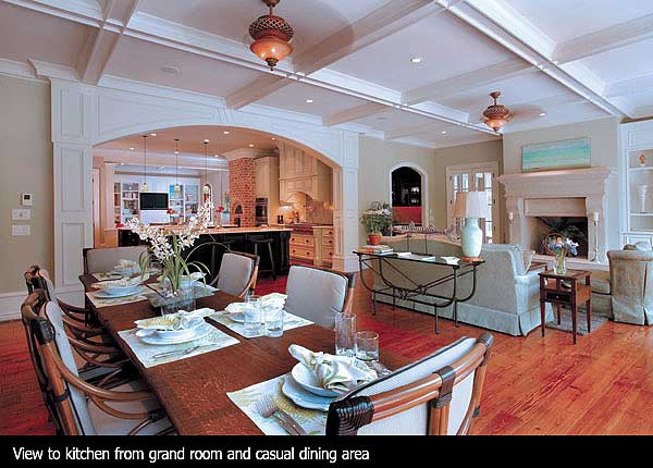 View from dining room to kitchen, showing coffered ceiling, arched entryway, fireplace, and sofa.