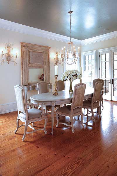 Dining room with oval table, upholstered chairs, ornate mirror, and French doors. Features chandelier and sconces.