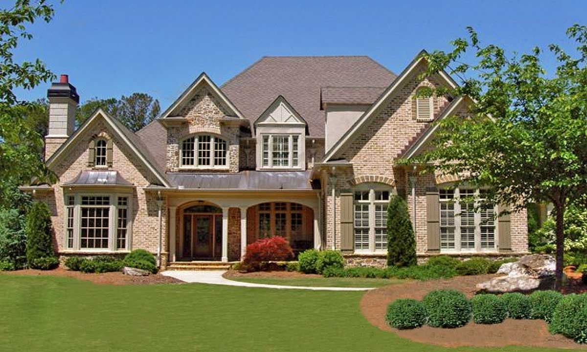 House plan exterior: Two-story brick home with arched windows, dormers, stone accents, and a covered entry.