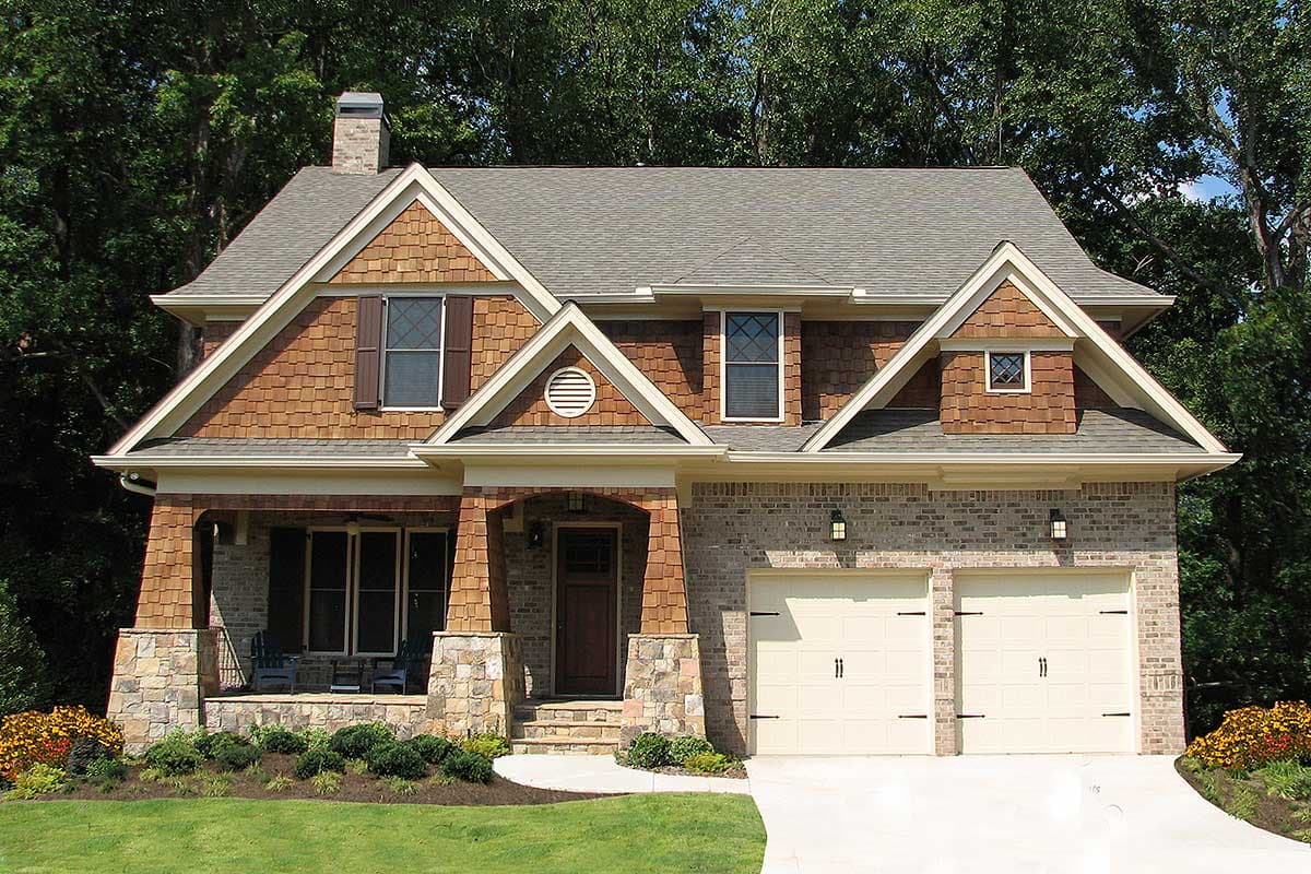 House plan exterior: Two-story home with brick and cedar shake siding, covered front porch with stone pillars, and a side-entry two-car garage.