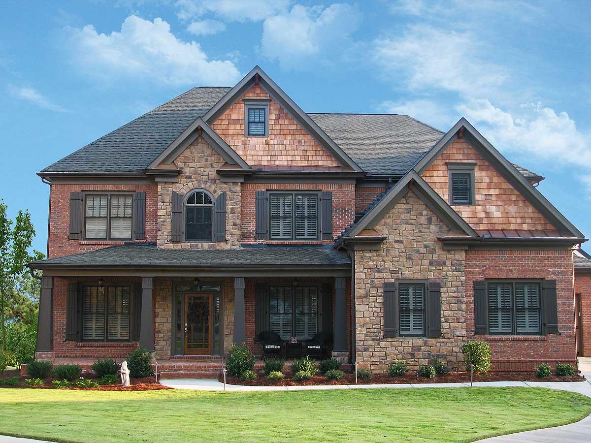 House plan exterior: Two-story brick and stone home with shingle accents, wide covered porch, gables, and arched window.