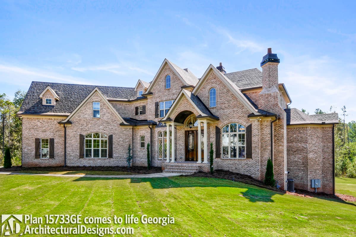 House plan exterior: Two-story brick home with arched windows, dormers, multi-level gables, and a covered entryway with columns.