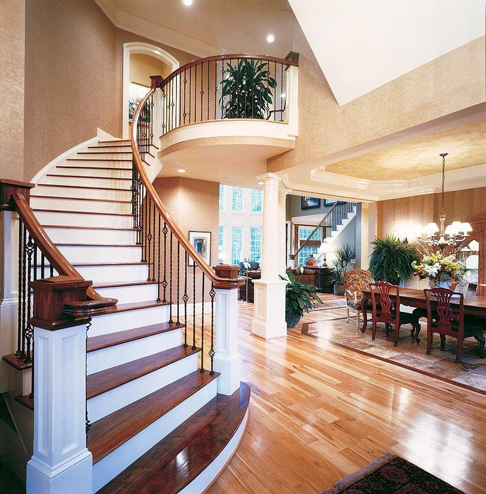 Interior view of a grand foyer with a curved staircase, balcony overlook, and adjacent dining room.