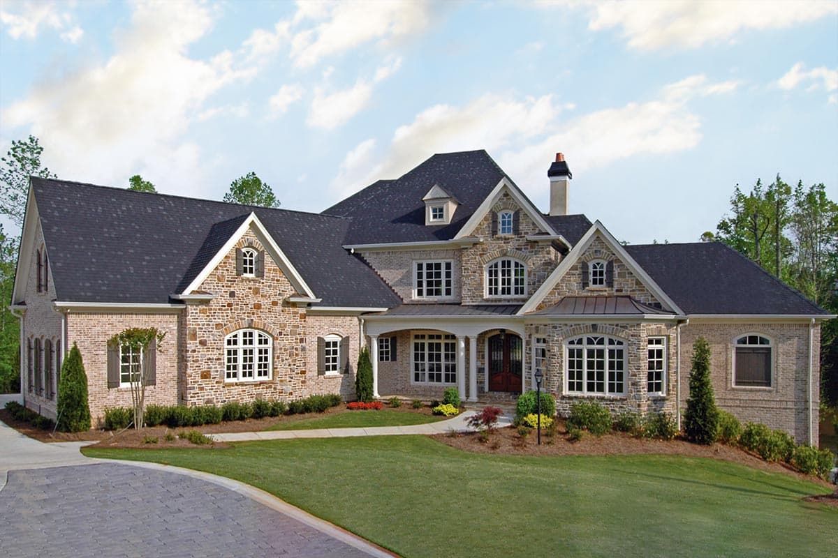 House plan exterior: Two-story home with brick and stone facade, prominent gables, arched windows, and covered entry.