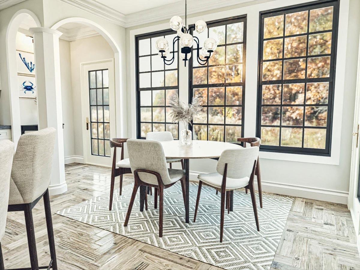 Dining area with round table, chairs, large grid windows, arched entryway with door and columns.