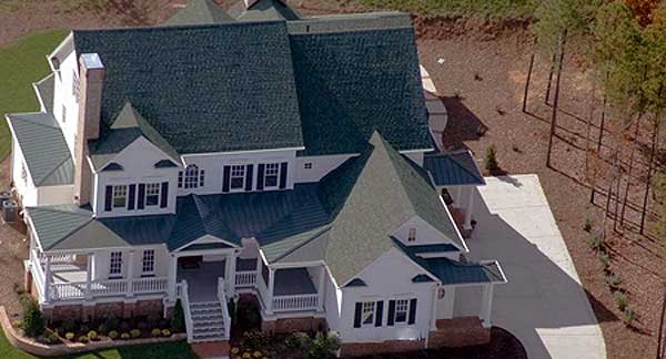 House plan exterior: two-story residence with green metal roof, multiple gables, and wrap-around porch.