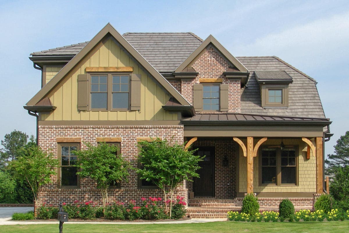 House plan exterior. Two-story Craftsman home with a gabled roof, brick facade, and covered front porch with exposed rafters.