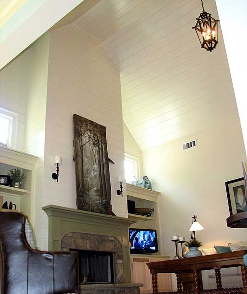Interior view of great room with vaulted shiplap ceiling, stone fireplace, built-in shelving, and large windows.