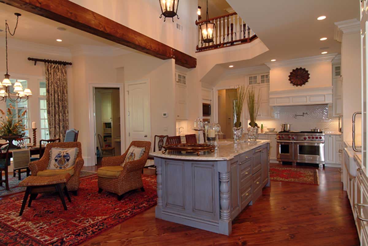 Open concept living area with kitchen island, vaulted ceiling with exposed beams, and upper level balcony.