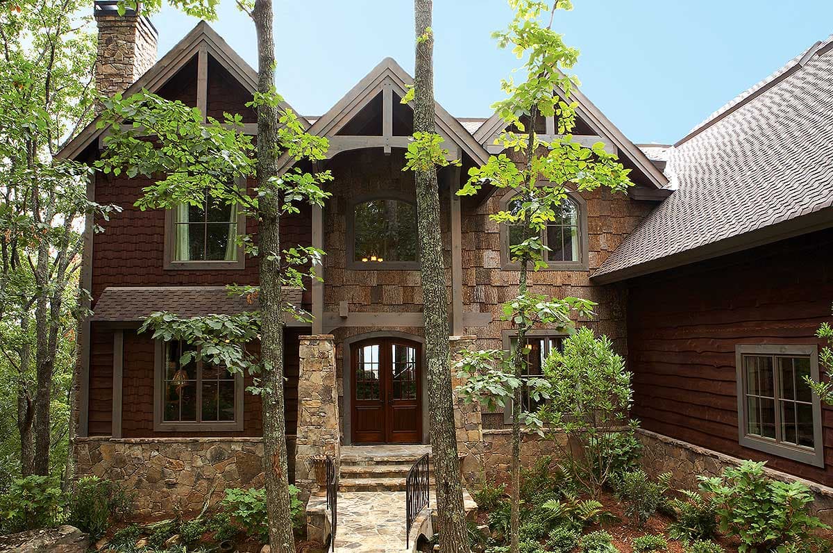 House plan exterior with stone and wood siding, prominent gables, arched windows, and a covered entry with double doors.