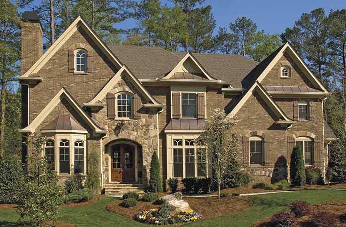 House plan exterior featuring brick and stone facade, arched windows, gables, and covered entryway.