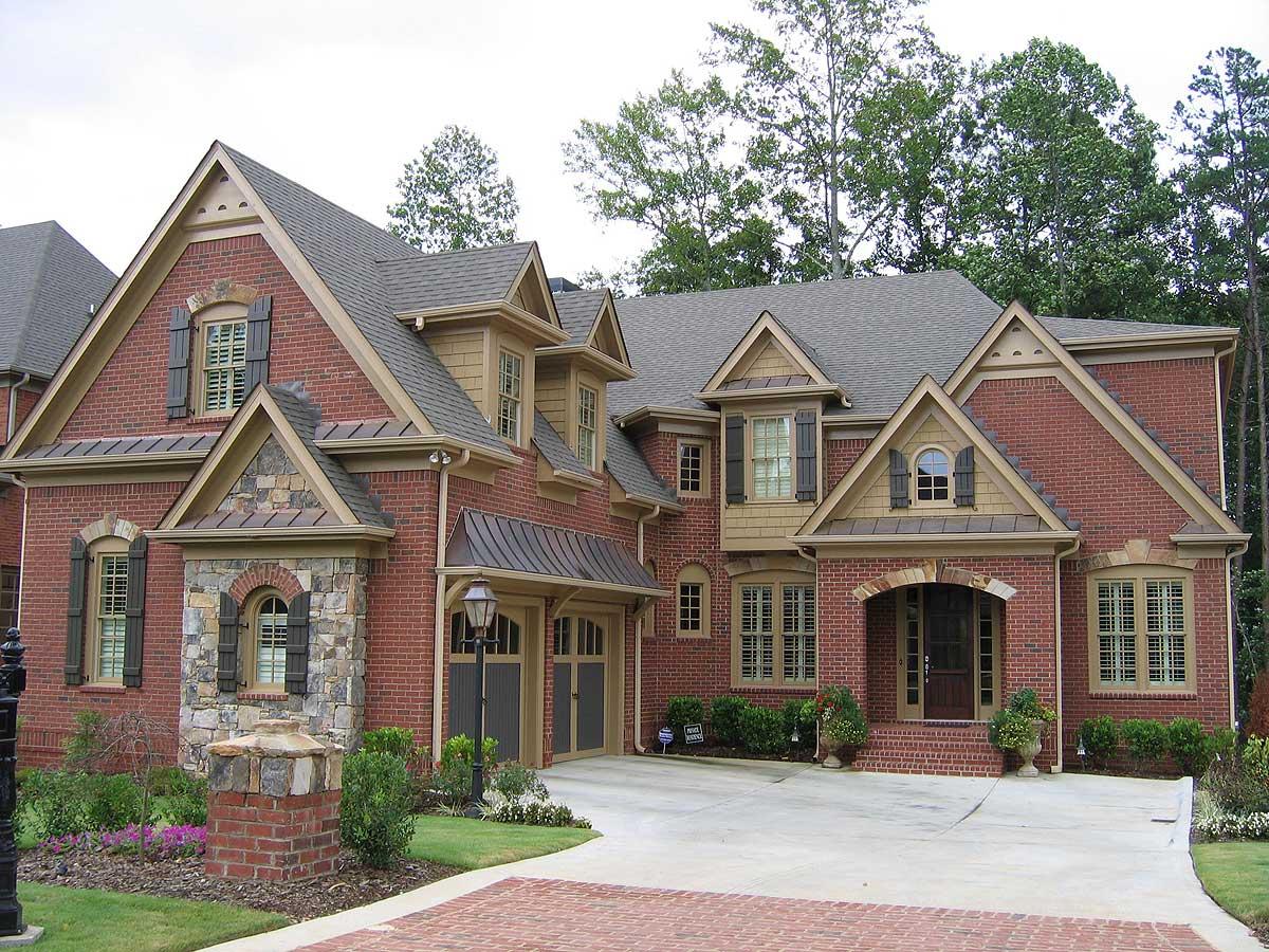House plan exterior: Two-story brick home with stone accents, multiple gables, dormers, arched entry, and side-entry garage.