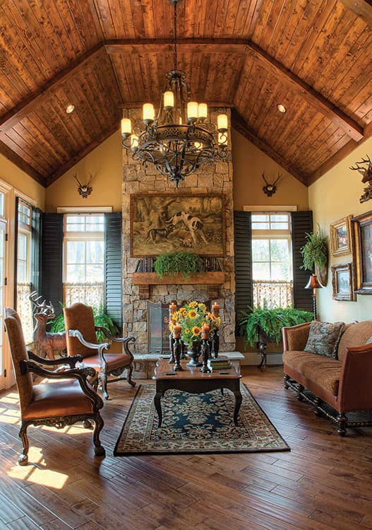 Interior view of a living room with a stone fireplace, vaulted wood ceiling, and a large chandelier.