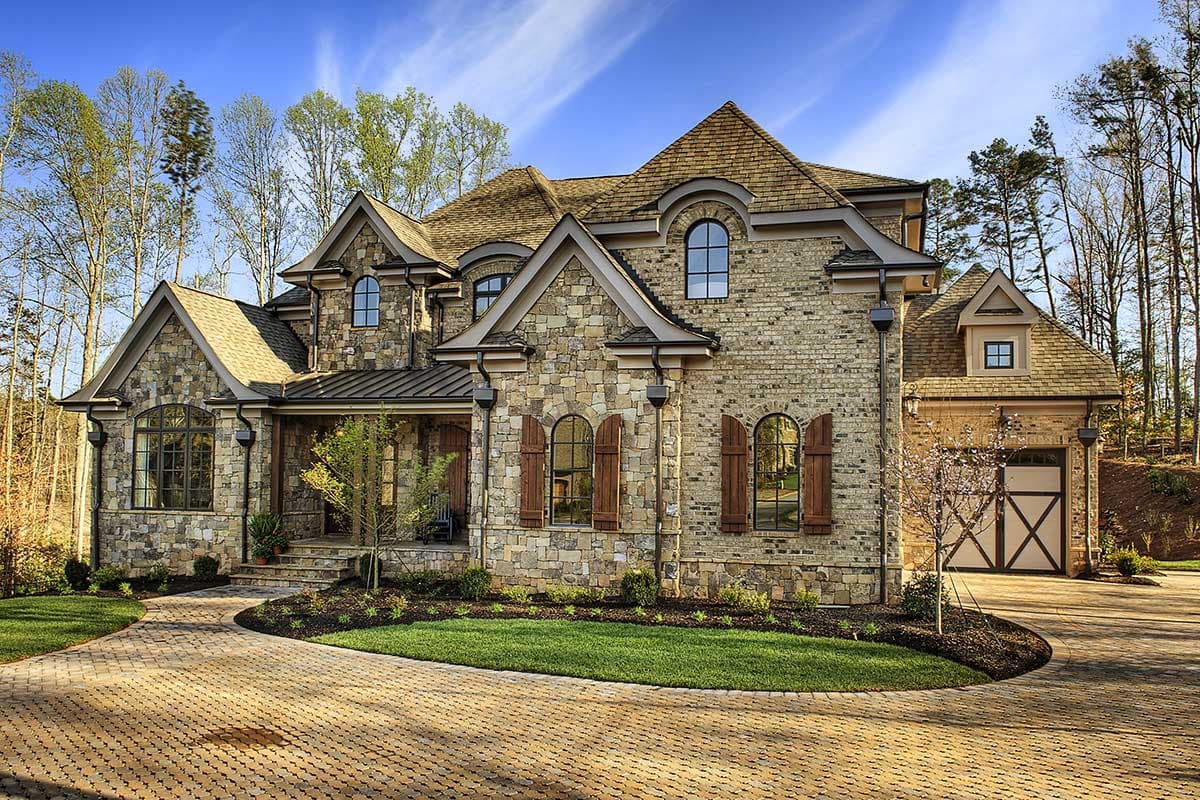 Exterior house plan: Two-story residence with stone and brick facade, arched windows, dormers, gables, and a side-entry garage.