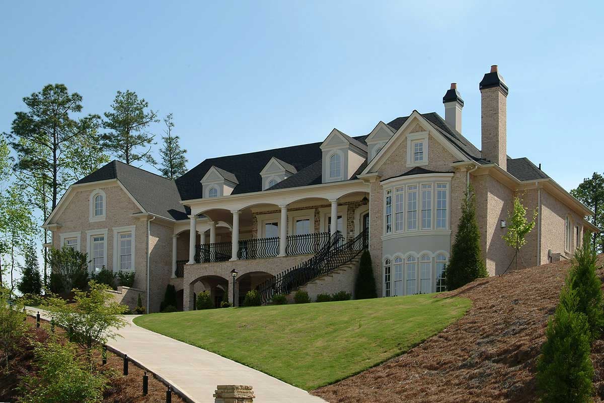 House plan exterior: large brick home with covered portico supported by columns, multiple gables, dormers, and bay windows.