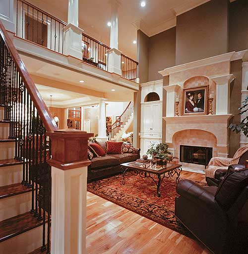 Open-concept living area with two-story ceiling, ornate fireplace, grand staircase, and second-story balcony.