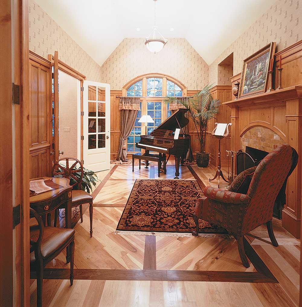 Music room with grand piano, fireplace, vaulted ceiling, arched window, and inlaid wood flooring.