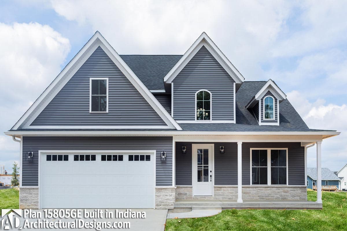 House plan exterior: two-story, gray vinyl siding, gable roof, prominent gables, arched dormers, attached garage, covered front porch.