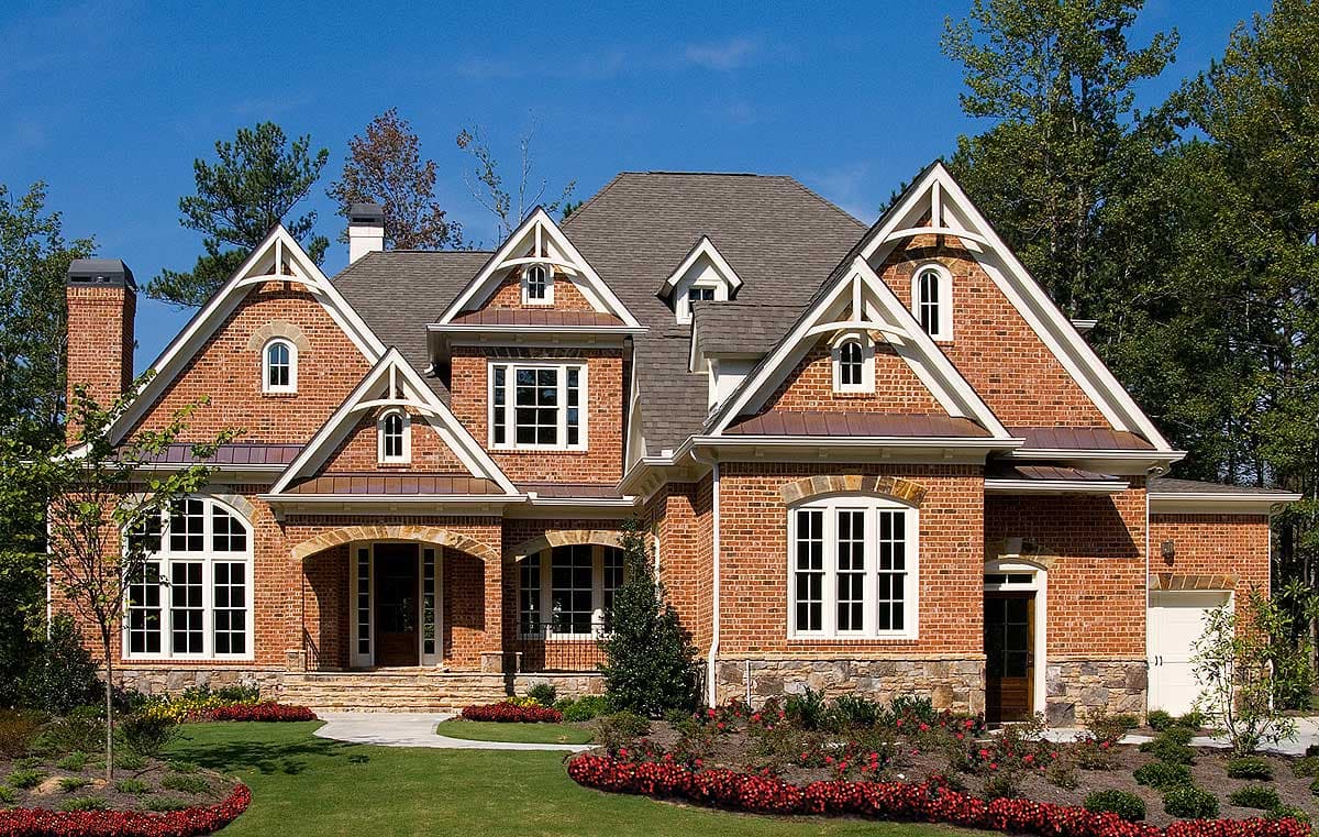 House plan exterior with brick facade, arched entry, multiple gables with decorative trim, copper roof accents, and a three-car garage.