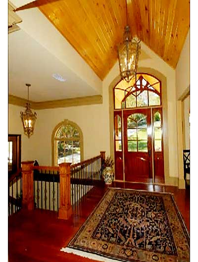 Interior foyer with vaulted wood ceiling, arched entryway with double doors, staircase with wood newel posts and metal balusters.