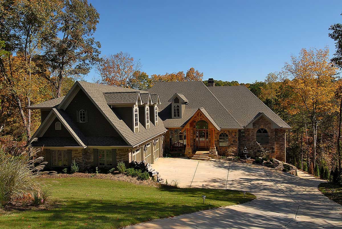 House plan exterior: Traditional style, multi-story home with stone accents, gabled dormers, and a covered entry with arched timber details.