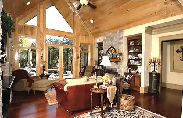 Great room with vaulted wood ceiling, stone fireplace, built-in bookshelves, and large windows.