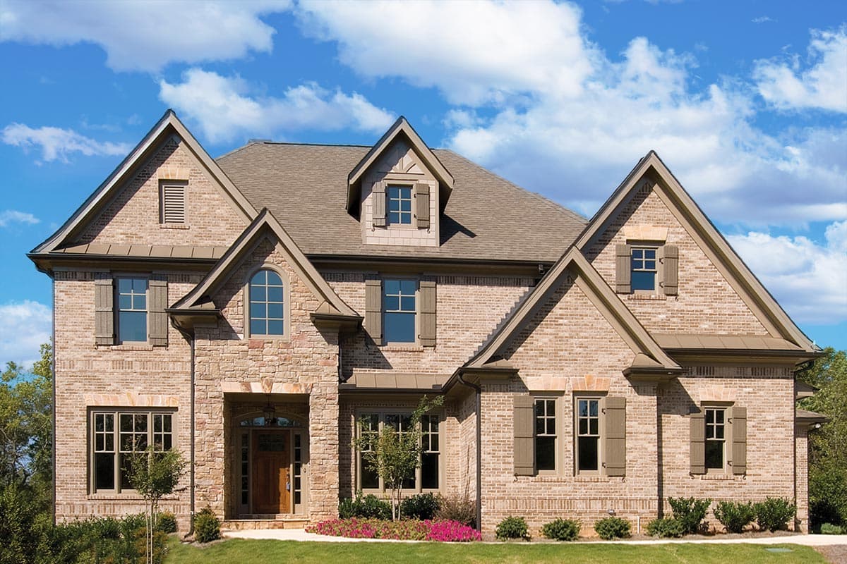 House plan exterior: Two-story brick home with stone accents, multiple gables, dormers, arched entryway, and decorative shutters.