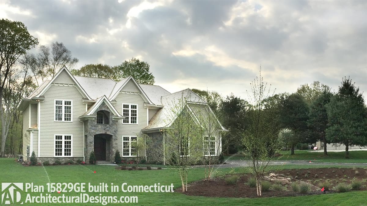 House plan exterior, two stories, shingle siding, stone facade, arched entryway, multiple gables.