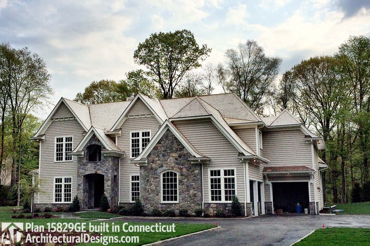 House plan exterior: Two-story home with stone accents, multiple gables, dormers, and a side-entry garage.