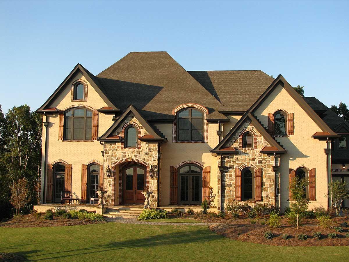 House plan exterior with stone accents, multiple gables, arched windows, wooden shutters, and a prominent arched entryway with double doors.