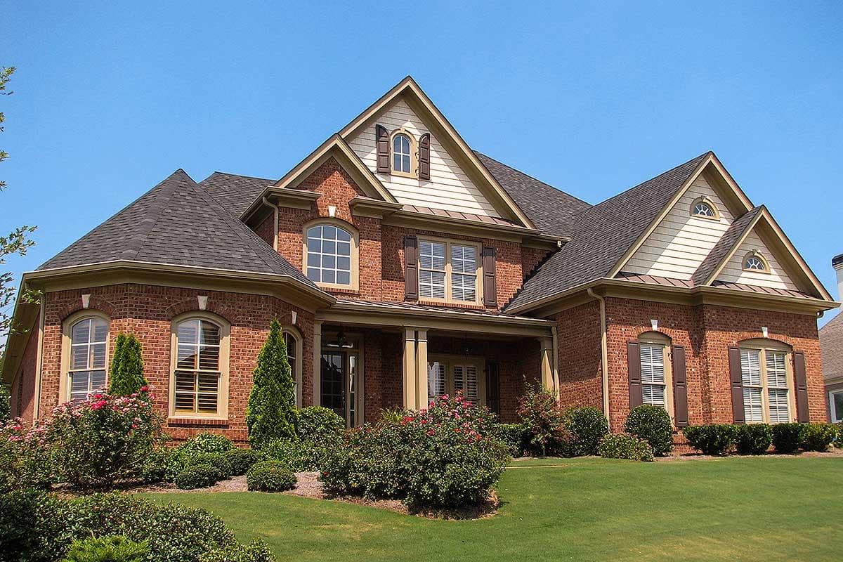 House plan exterior view of a two-story brick home with a covered porch, arched windows, and multiple gables.
