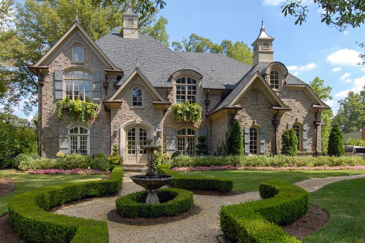 House plan exterior: Stone two-story home with multiple gables, arched dormers, cupola, and a central arched entryway with double doors.