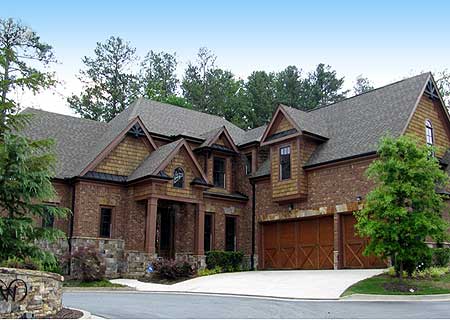 House plan exterior: brick and cedar shingle facade, multiple gables, prominent front entrance with columns, and a three-car garage.