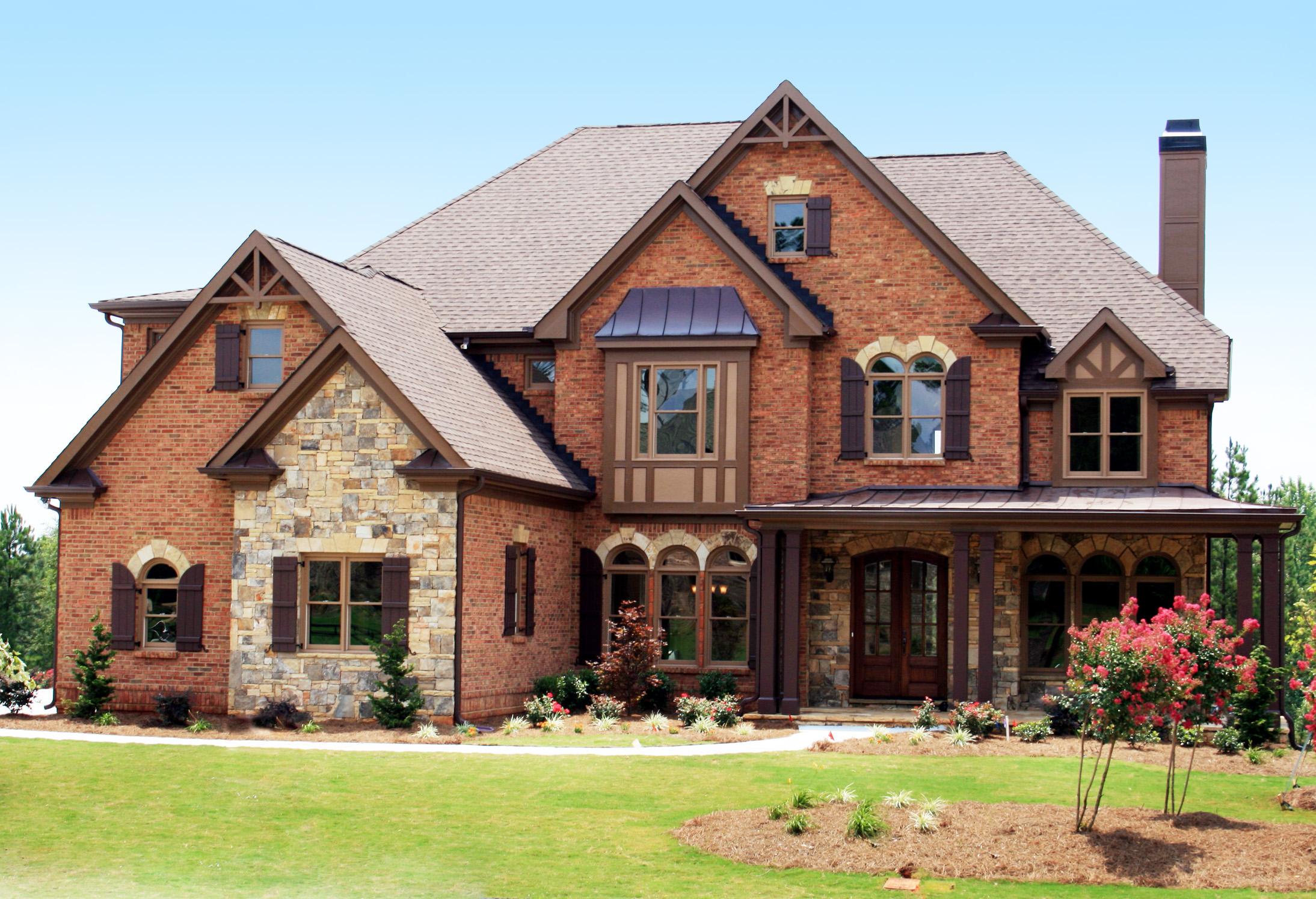 House plan exterior: Two-story brick and stone home with a prominent gabled entrance, bay window, and arched windows.