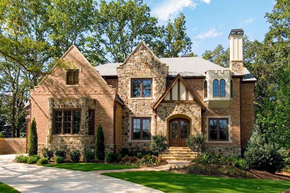 House plan exterior: Tudor style home with stone and brick facade, multiple gables, arched entry, and bay window.