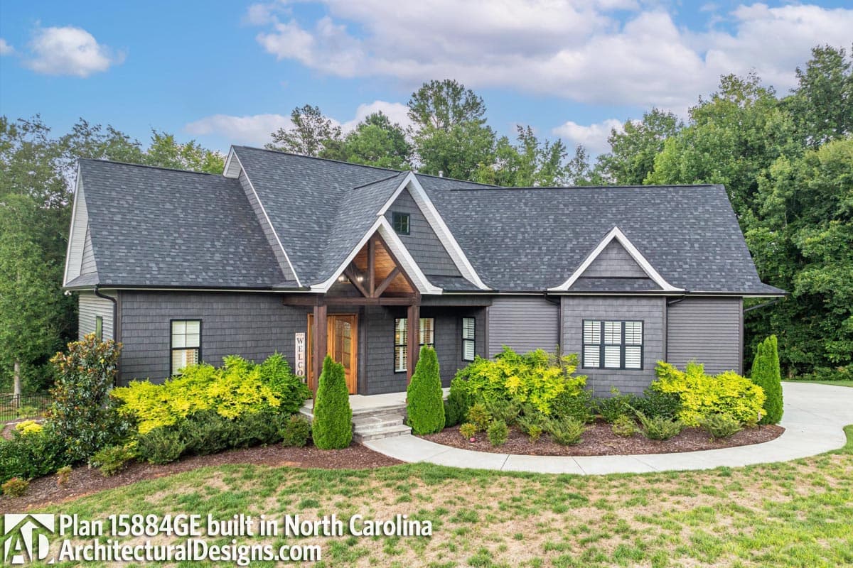 House plan exterior with dark siding, multiple gables, wood-trimmed entryway, and a prominent roofline.