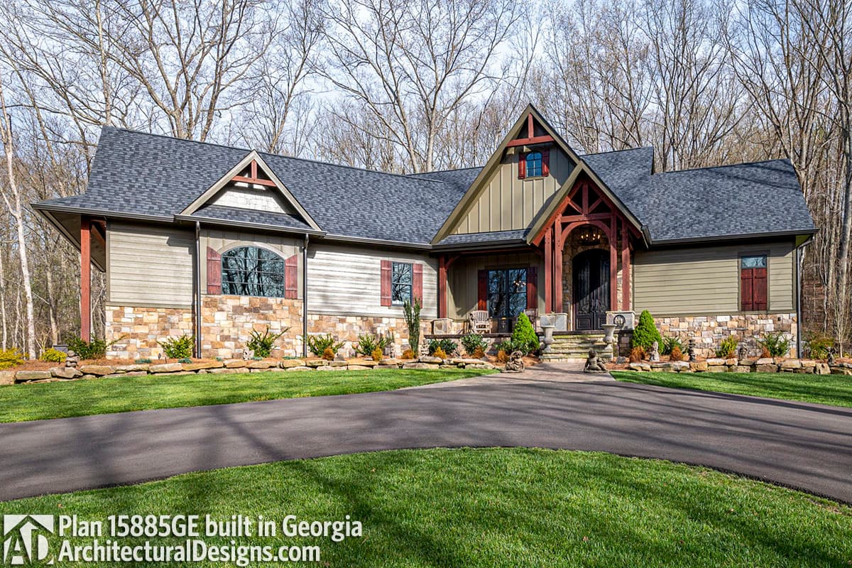 House plan exterior: Two-story lodge-style home with stone foundation, board-and-batten siding, prominent gables, and arched entry.