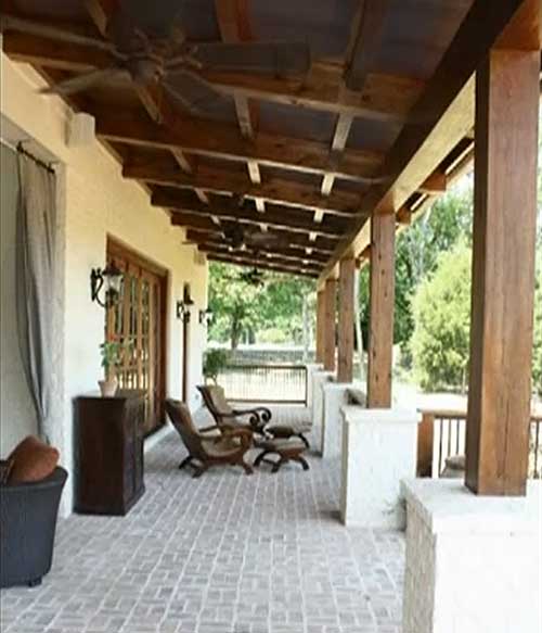 House plan exterior: Covered patio with exposed timber beams, ceiling fans, brick flooring, and large wooden posts.