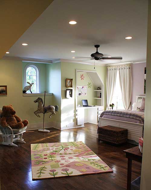 Bedroom interior with bed, desk, rocking chair, arched window, and rug. Ceiling fan and recessed lights.