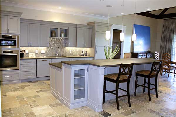 Kitchen with gray cabinets, stainless steel double oven, large island with seating, and stone tile flooring.