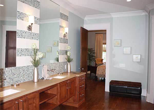 Bathroom vanity with double sinks, wood cabinetry, and mosaic tile backsplash, opens to bedroom.