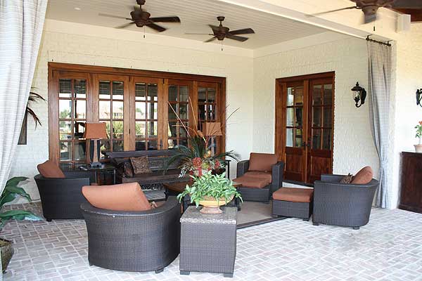 Covered outdoor living space with brick floor, ceiling fans, and wood-framed glass doors.